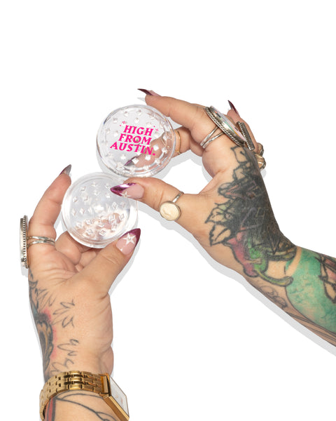 Two hands with tattoos holding small acrylic grinder and 'High From Austin' text.